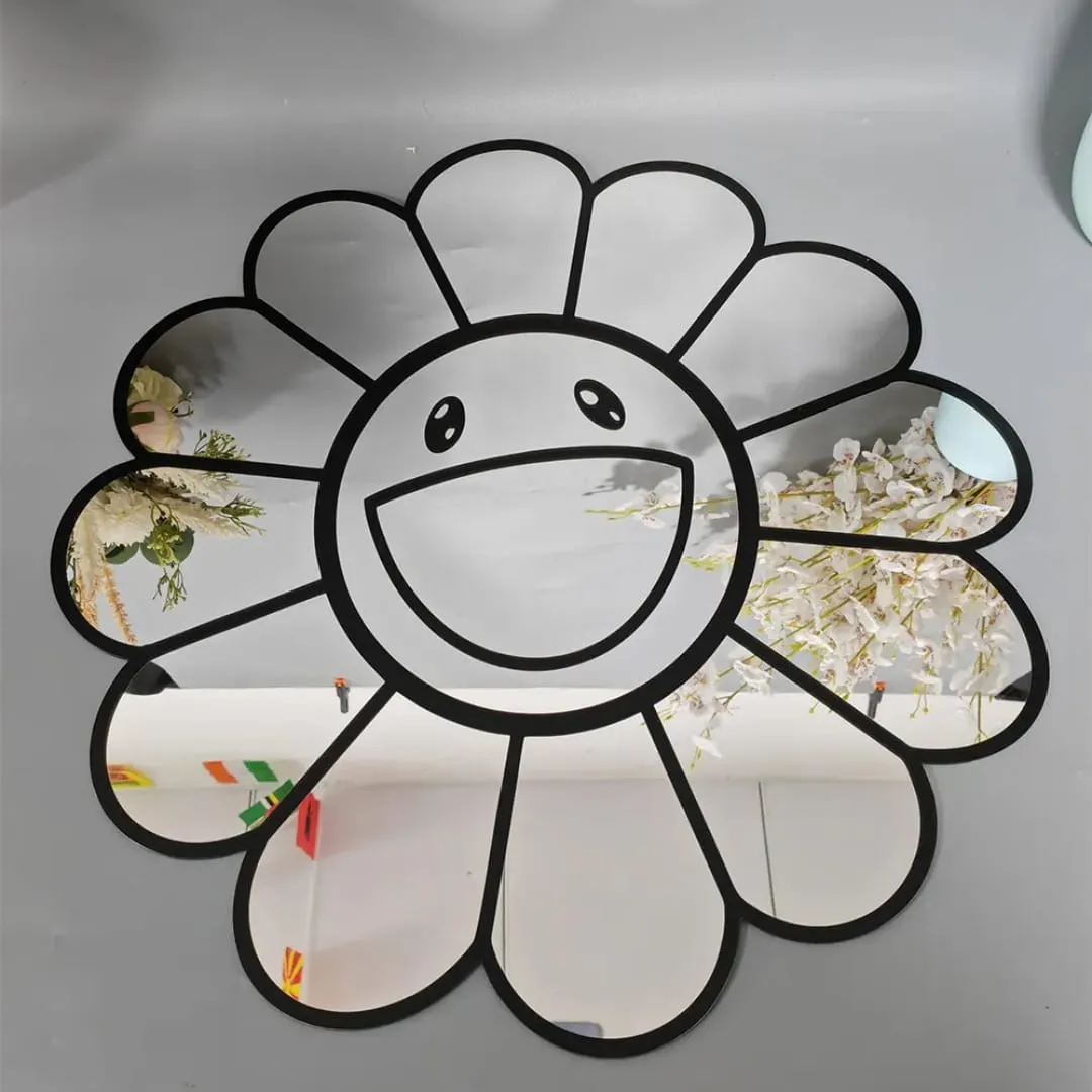 Straight-on view of the cute smiley daisy mirror resting against a light grey wall, reflecting white floral branches and bright room lighting across its glass petals.