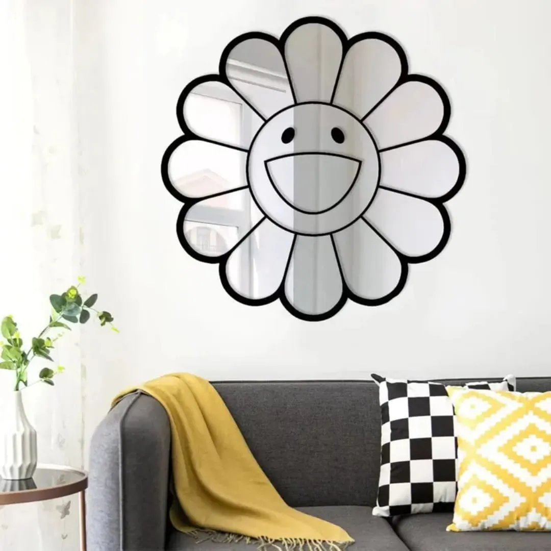 The smiley daisy mirror hung on a white wall above a grey sofa styled with a yellow throw blanket and patterned pillows, reflecting a bright window and natural light.
