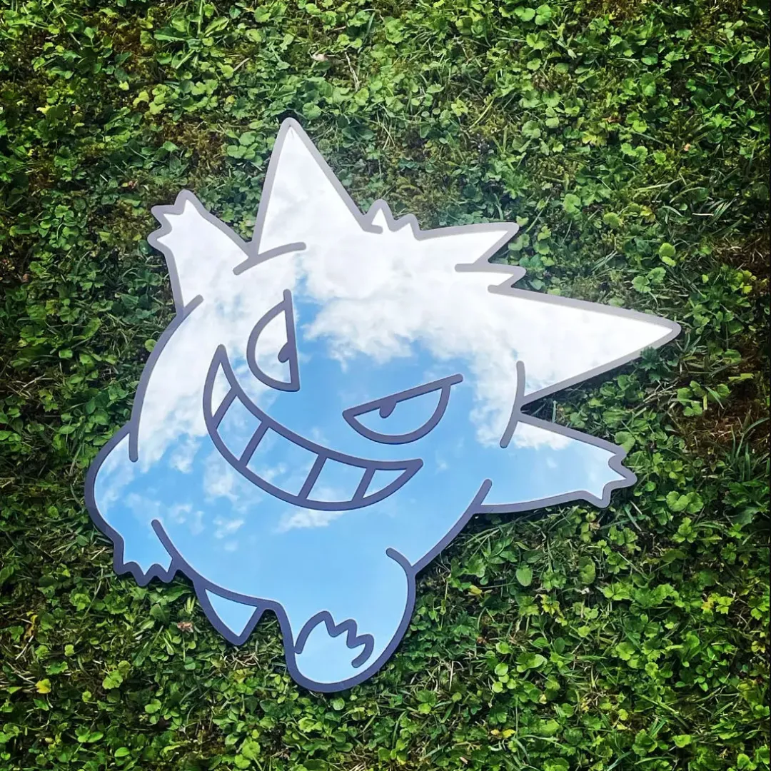 Straight-on view of the round Spooky Ghost Mirror resting on a white surface against a plain wall, featuring the white ghost decal and reflecting a modern light fixture.