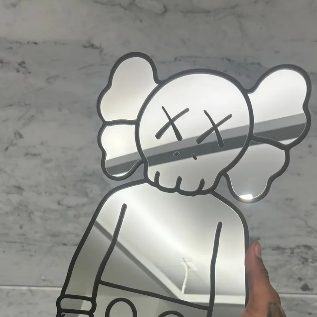 Close-up view of a hand holding the Street Bear mirror against a marble wall, highlighting the character's distinctive X-eyes and skull-like face design while reflecting the room's ceiling.