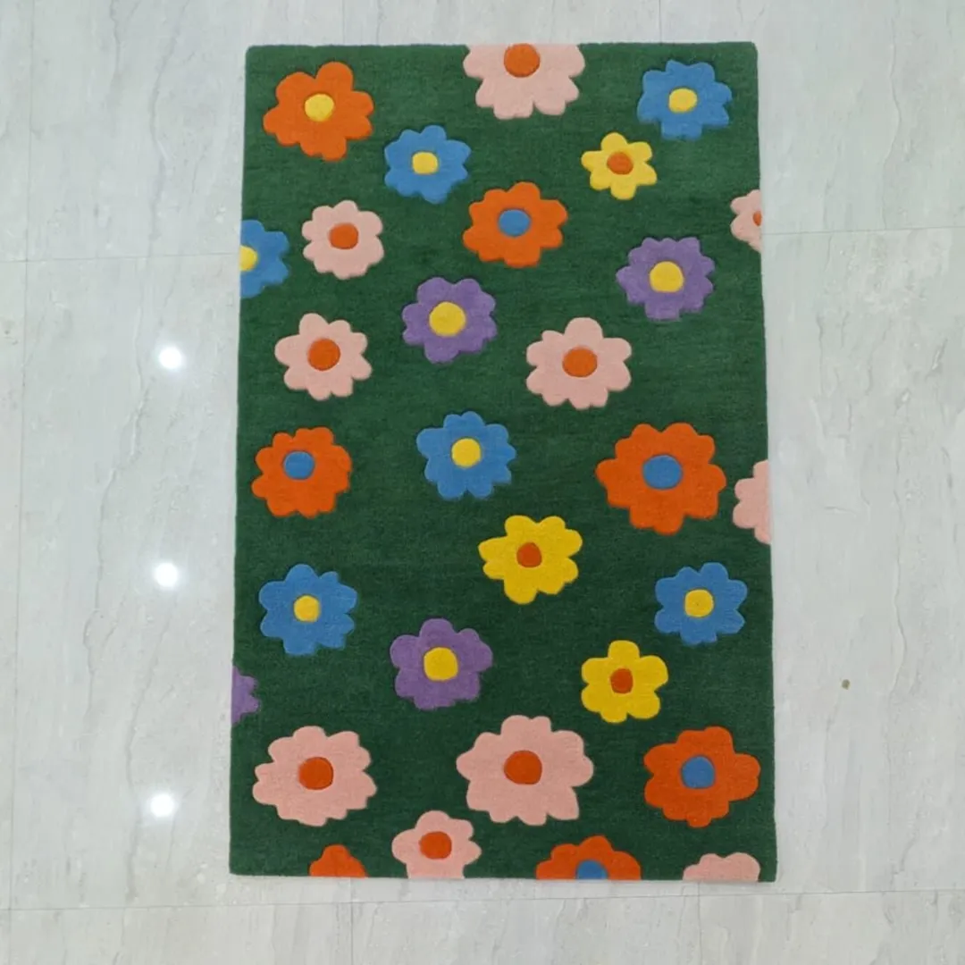Full overhead shot of the rectangular Daisy Bloom Rug laid completely flat on a light grey tiled floor. The design showcases a repeating pattern of bright, multicolored tufted daisy flowers on a solid dark green background.