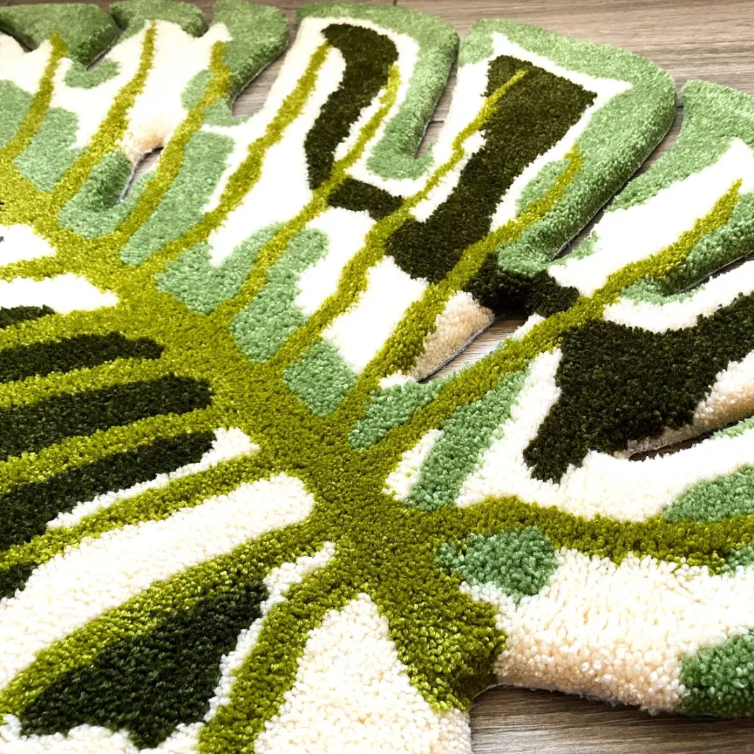 Close-up view of the Verdant Monstera Rug's scalloped outer edges, showing the intricate cut-out leaf details and the dense, high-quality tufted yarn in cream, dark green, and light green shades.