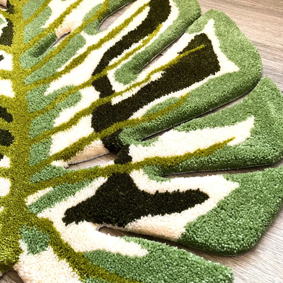 A detailed close-up of the Verdant Monstera Rug, highlighting the thick tufted texture of the central bright green vein intersecting with plush cream, light green, and dark green leaf patterns.
