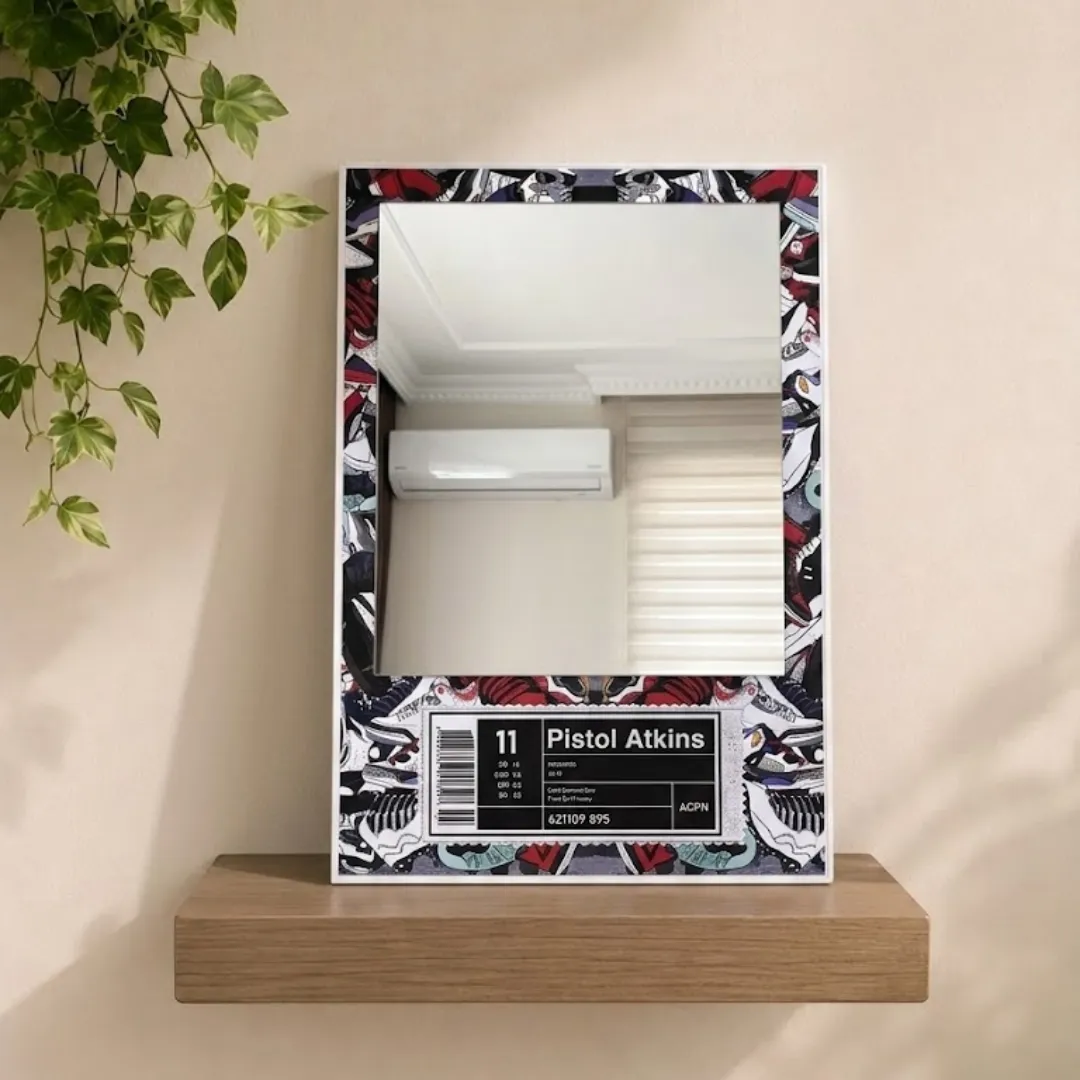 A studio shot of the "Pistol Atkins" sneaker-themed mirror displayed on a minimalist light wood floating shelf against a neutral wall with trailing greenery.