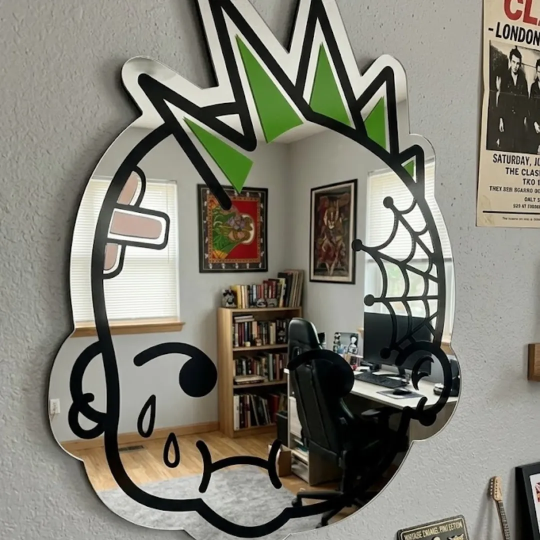 Crown designer punk character wall mirror styled in a room with a bookshelf, desk, and framed posters on the wall.