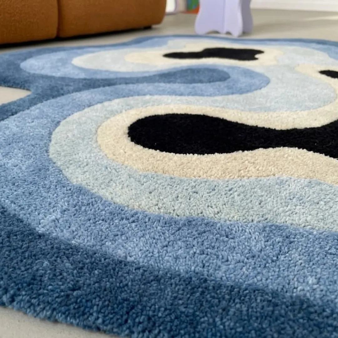 Close-up of the plush tufted pile texture, flowing blue gradient layers, and bold black shapes on the Deep Tide rug.