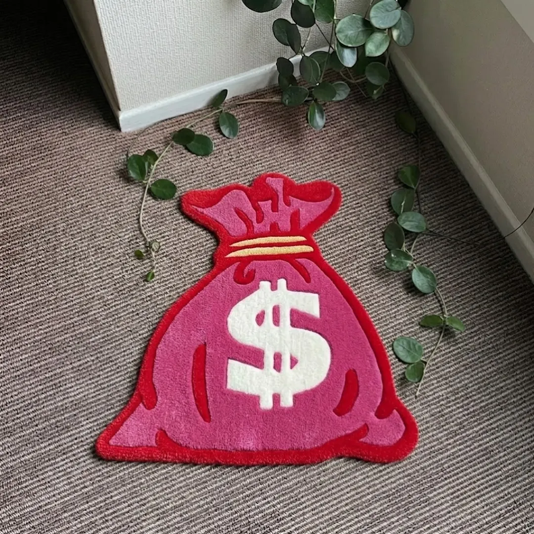 dollar bag rug top view Dollar Bag handmade tufted area rug featuring a money sack design in pink, red, and white with a dollar sign symbol, displayed flat on a carpeted floor.