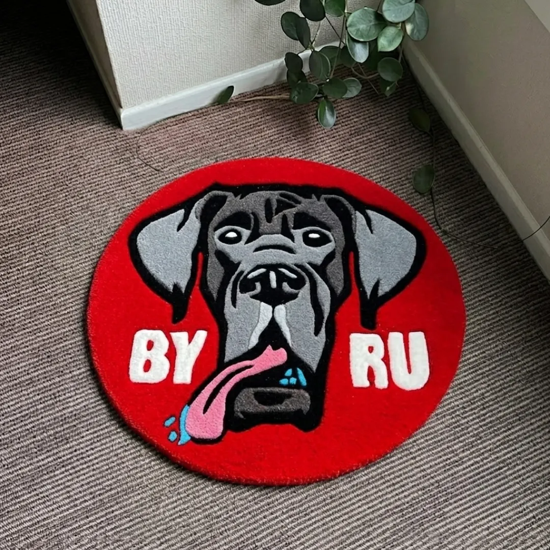 drooly duke rug overhead view Drooly Duke handmade tufted circular area rug featuring a gray dog portrait with a pink tongue sticking out and white text on a bright red background, displayed flat on a carpeted floor.