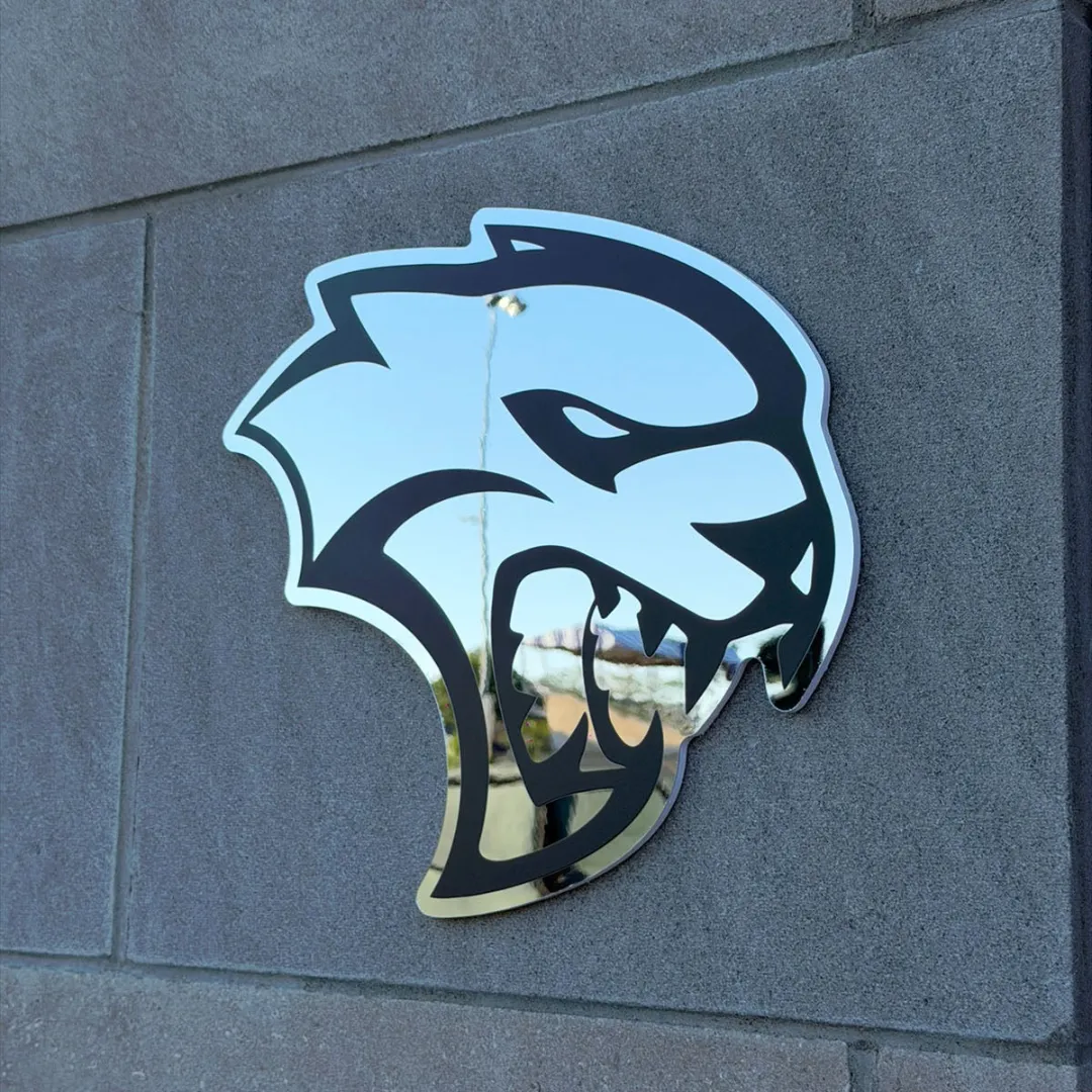 Falcon Edge shaped wall mirror mounted on a textured grey stone block wall reflecting an outdoor environment.