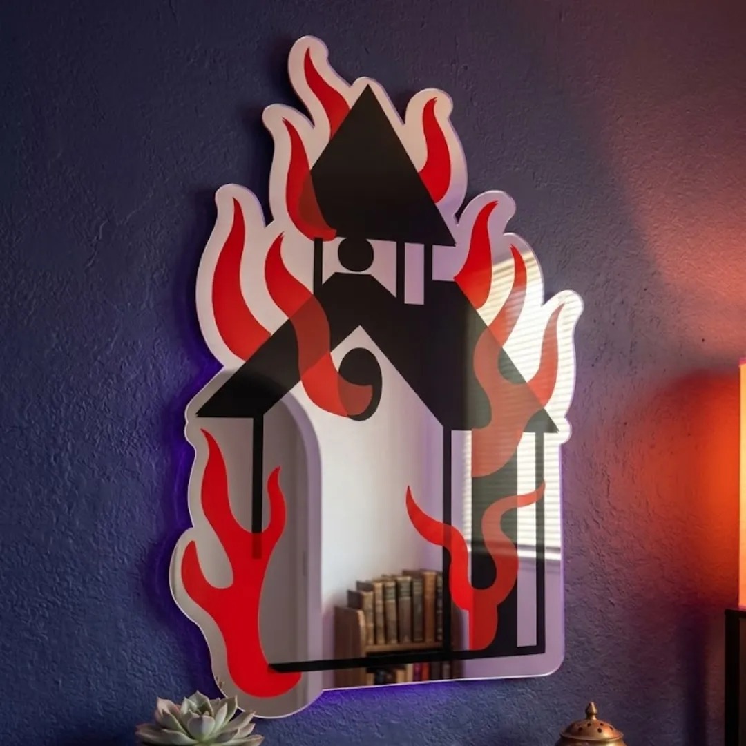 Ignivar Flame novelty burning church wall mirror styled in a room with a pink wall and framed art prints nearby.