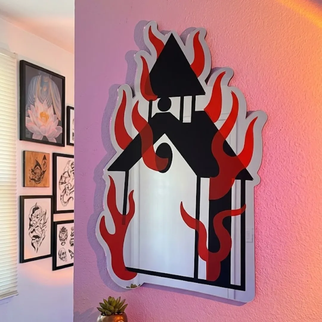 Ignivar Flame decorative wall mirror featuring a burning church design with red flames and black silhouette outlines, mounted on a dark textured wall.