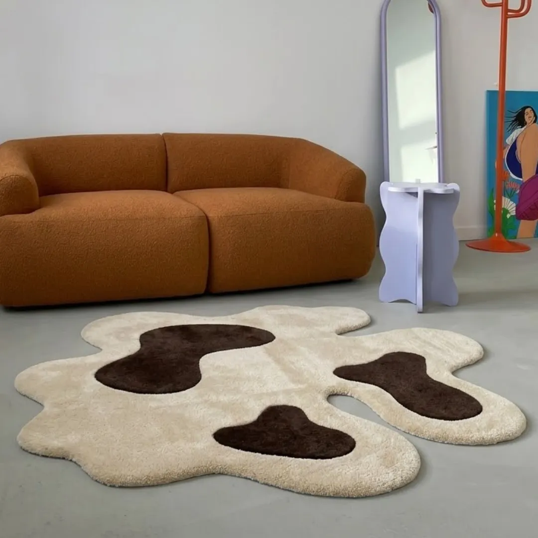 oat muse rug room mockup Oat Muse abstract cow-print area rug styled in a modern interior space with a warm brown sofa and contemporary decor.