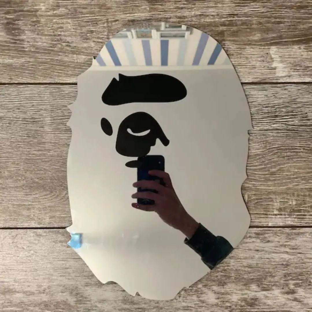 Shadow Face decorative wall mirror featuring an ape head silhouette design, displayed flat against a rustic wooden background.