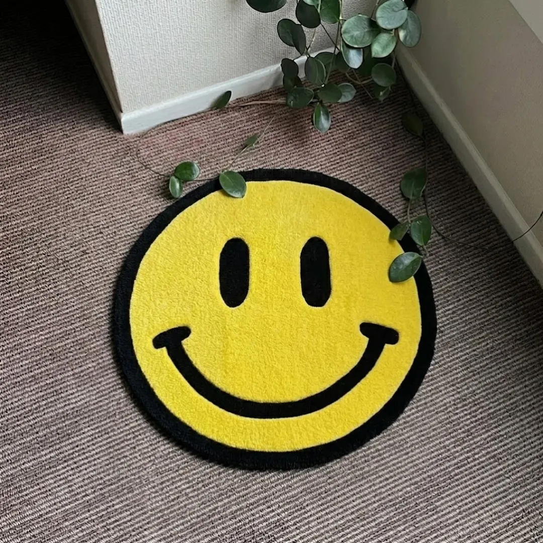 solvani smile rug top view Solvani Smile handmade tufted area rug featuring a classic yellow and black smiley face design, displayed flat on a carpeted floor.