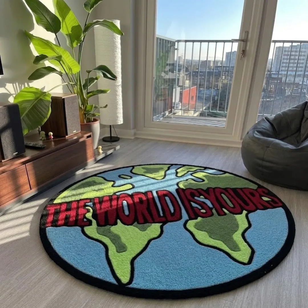 the world is yours rug angle room mockup Angle view of The World Is Yours designer globe rug laid out on a light wood floor next to a media console, indoor plant, and window.