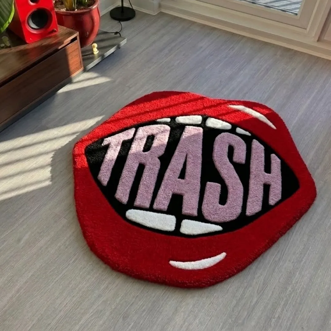 trash lips rug living room mockup Trash Lips handmade tufted area rug featuring an open mouth design with red lips, white teeth, and the word "TRASH" styled on a light wood floor.