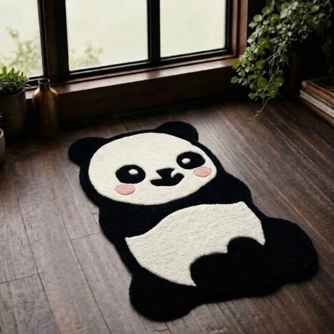 oreo puff rug overhead floor view Oreo Puff handmade tufted novelty area rug shaped like a cute cartoon panda with pink cheeks, displayed flat on a dark wooden floor near a window.